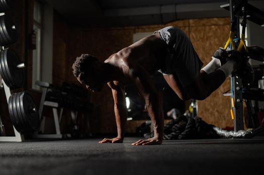 Shirtless afro american man doing exercises with functional loops in the gym