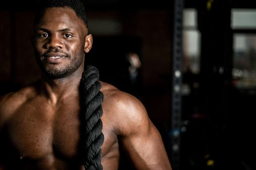 Muscular african american man posing with rope in gym