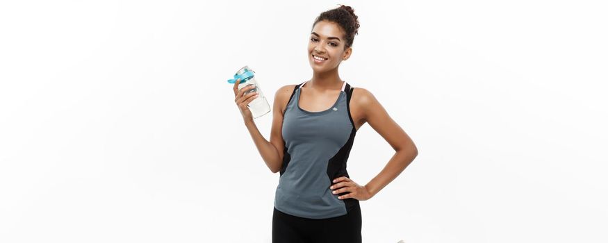 Healthy and Fitness concept - beautiful African American girl in sport clothes holding water bottle after workout. Isolated on white studio background.