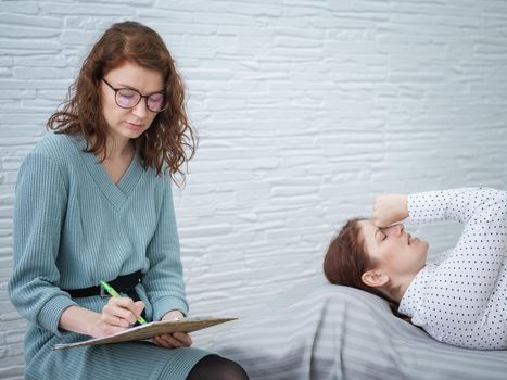 A caucasian woman lies on a couch and expresses her feelings, while a psychologist makes notes on a tablet