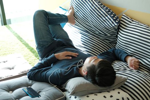 asian male teenager man listening to music from smart mobile phone while lying on floor at home