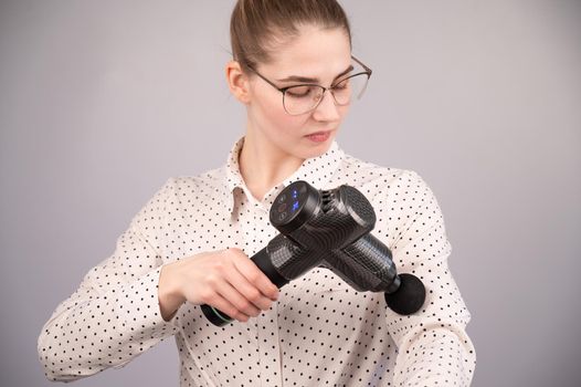 Caucasian business woman massaging her biceps with a percussion massager