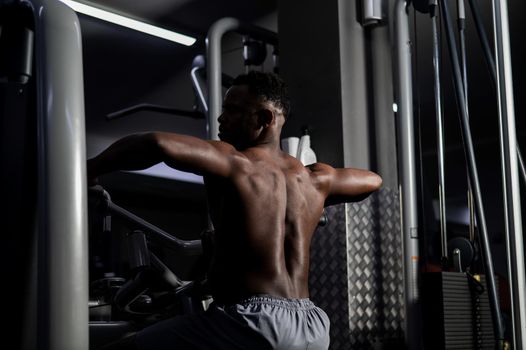 Shirtless african american man doing back exercises on a machine in the gym