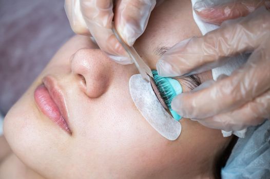 The master combs the eyelashes of a woman with a fish applicator