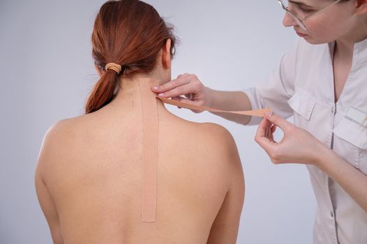 Female doctor glues kinesio tapes on the patient's shoulder