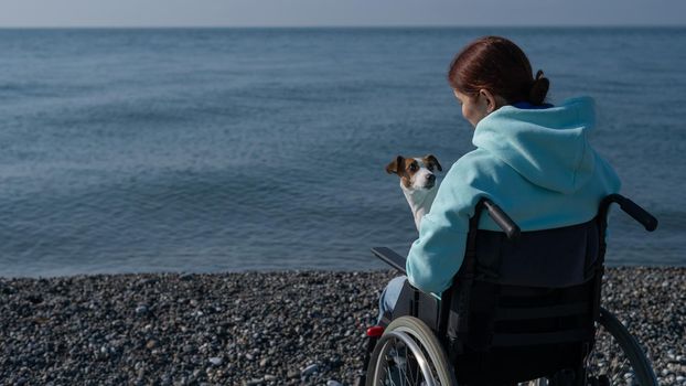 Caucasian woman in a wheelchair cuddling with a dog near the sea