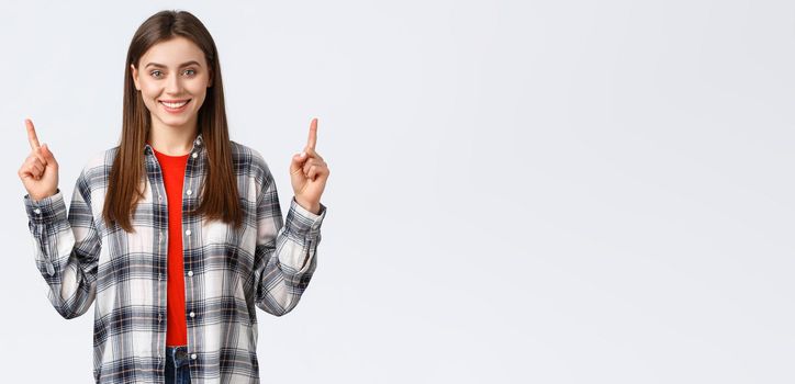 Lifestyle, different emotions, leisure activities concept. Confident smiling girl in checked shirt, turn attention to upper banner, pointing fingers up and look camera, telling about advertisement.