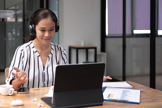Happy asian young wearing headset, communicating with client via video computer call..