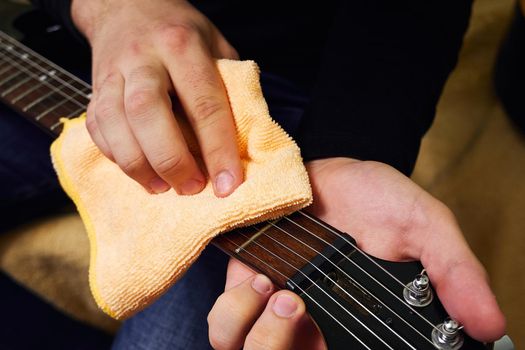 Hands of a man wiping the fretboard of an electric guitar with a special cloth