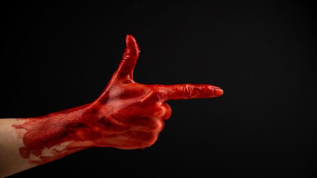 Woman's hand in blood shows a gesture of a gun on a black background