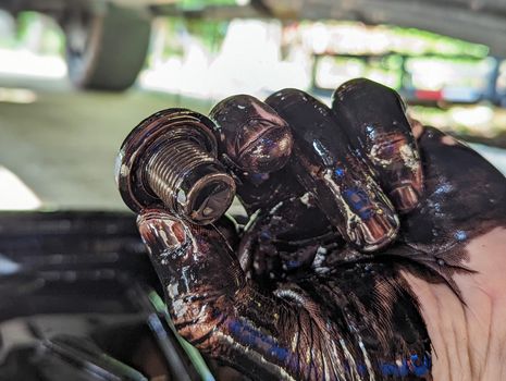 view of auto mechanic with mud on hands changing car oil