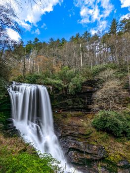 A scenic waterfall roadside going over the cliff down to the boulders and rocks below where you can no longer drive under but can walk underneath the raging waters