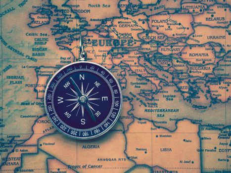 The compass is placed on the ancient or vintage world map between Europe continent and Africa continent. Travel geography navigation concept background.