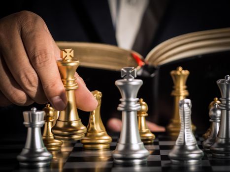 Hand of businessman moving the golden king chess to fighting silver king chess with opening book guideline play successfully in the competition. management or leadership strategy and teamwork concept.