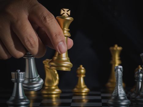 Hand of businessman holding gold king checkmate silver king on chess board to successfully in the competition. Management or leadership strategy and teamwork concept.