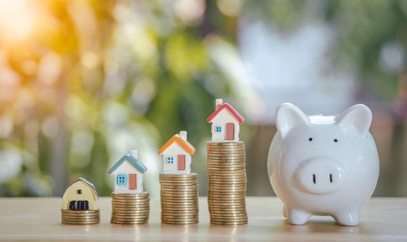 Coins stack 4 rows of gold coins and a white piggy bank placed on a wooden table to save money invest for future. Concept for loan, property ladder, financial, real estate investment, taxes and bonus.