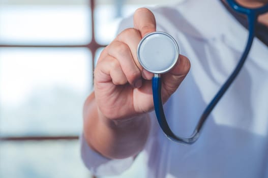 Male medicine doctor hand holding stethoscope against of chest on hospital background. Physician ready to examine patient. Medical and patient care concept.