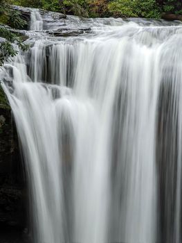 A scenic waterfall roadside going over the cliff down to the boulders and rocks below where you can no longer drive under but can walk underneath the raging waters