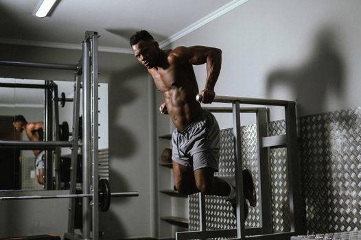 Handsome afro american man doing parallel bars exercise in gym