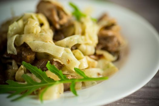 Homemade boiled noodles with meat and eggplant in a plate on a wooden table