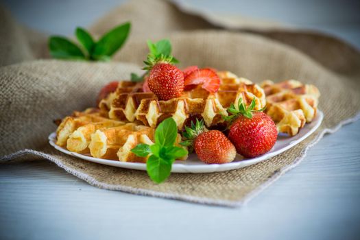 Sweet curd cooked waffles with fresh ripe strawberries, on a wooden table.