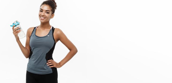 Healthy and Fitness concept - beautiful African American girl in sport clothes holding water bottle after workout. Isolated on white studio background.