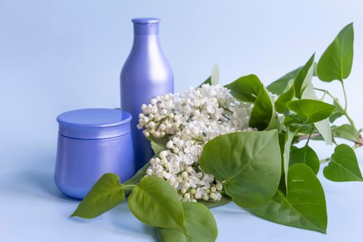 Two purple jars with cosmetic products and creams with fresh, blooming and fragrant lilac flowers and free space for advertising.