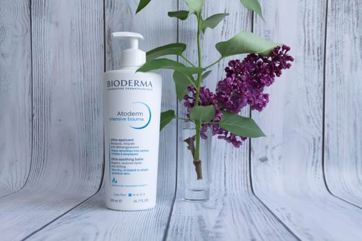 Bioderma dry skin care balm with a bouquet of purple lilac on a wooden background. Cosmetic products.