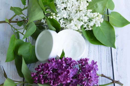 One white box with cosmetic products and creams with fresh, blooming and fragrant lilac flowers and free space for advertising.