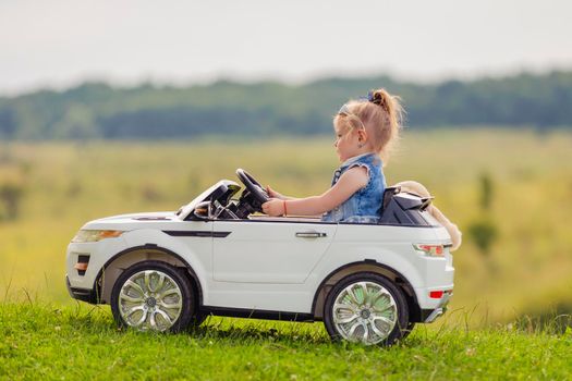 little girl rides on a children's car on a green lawn