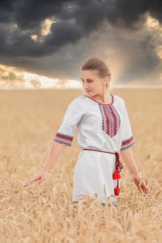 girl in the Ukrainian national costume on the background of a wheat field and sunset sun