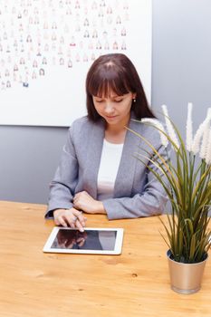 A brunette businesswoman in a gray jacket at her desk with a tablet in her hands. Business portrait in the office.
