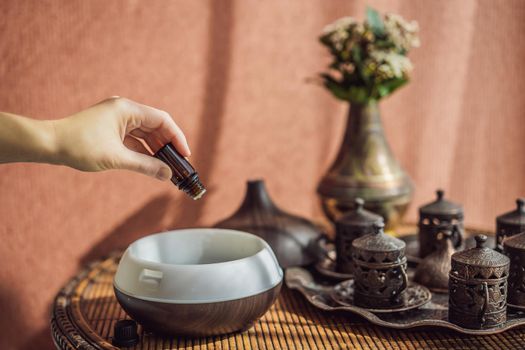 Woman adding essential oil to aroma diffuser on table.