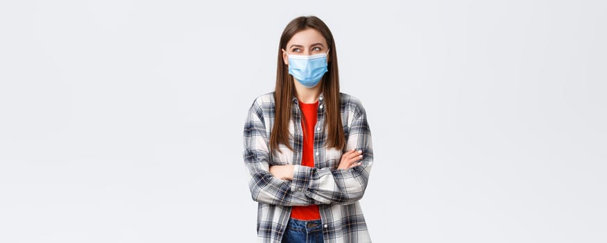 Coronavirus outbreak, leisure on quarantine, social distancing and emotions concept. Happy and dreamy young optimistic woman, beautiful girl in medical mask laughing and looking upper left corner.