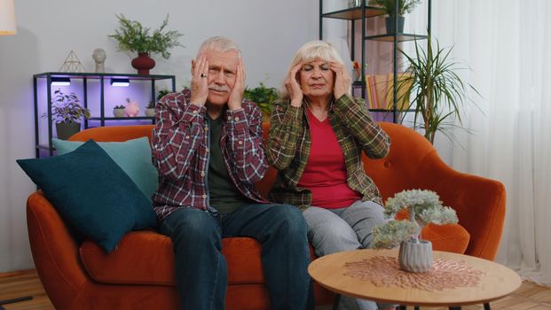 Displeased senior elderly family grandparents man woman rubbing temples to cure headache problem, suffering from tension and migraine, stress, grimacing in pain, high blood pressure on couch at home