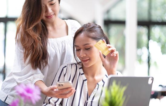 Asian two woman friend enjoy shopping online at cafe. Beautiful lesbian couple sit on sofa, holding credit card to make e bank online payment after use phone purchase goods in web store.