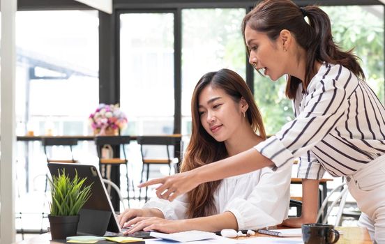 Two young beautiful asian business woman in the conversation, exchanging ideas at work..