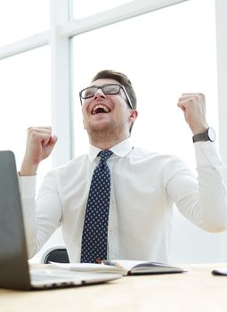 Happy young businessman raising hands in front of laptop