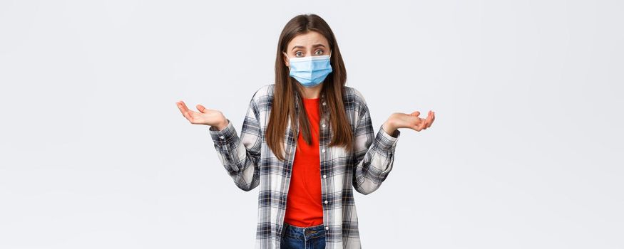 Coronavirus outbreak, leisure on quarantine, social distancing and emotions concept. Confused and indecisive young woman in medical mask dont know what do, shrugging with hands spread sideways.