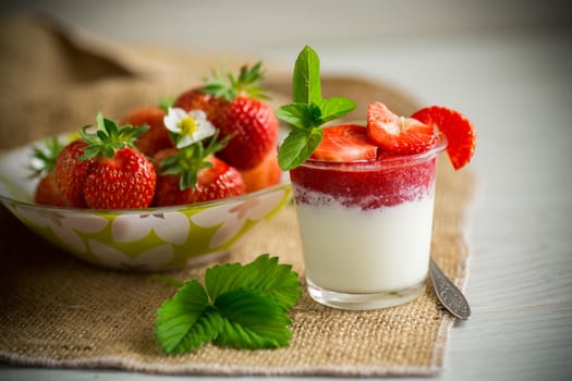 sweet homemade yogurt with strawberry jam and fresh strawberries in a glass cup, on a wooden table.