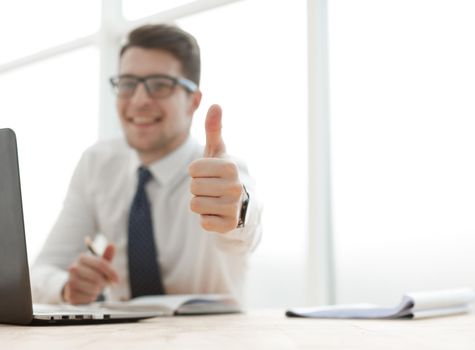 Cheerful young businessman standing and showing thumbs up in office