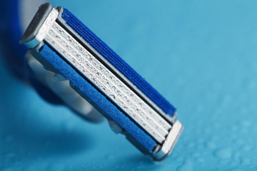 Shaving machine with three blades on a blue background with water drops in close-up. The concept of purity and freshness