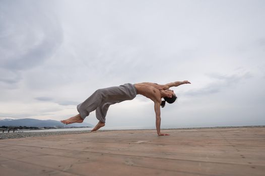 Shirtless caucasian man doing backflip on pebble beach