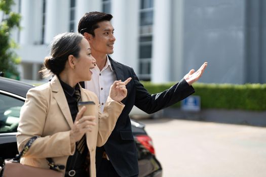 Happy senior old asian businesswoman discussion talking about new project with young asian male colleague at car park