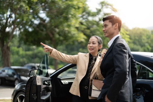 Happy senior old asian businesswoman discussion talking about new project with young asian male colleague at car park