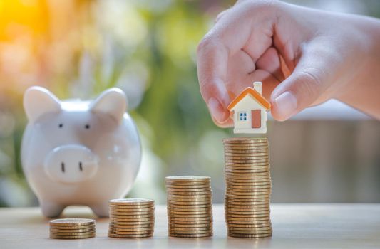Hand of boy holding home or house on gold coins stack and piggy bank to saving money invest for future and buy home.Concept loan, property ladder, financial, real estate investment and bonus.