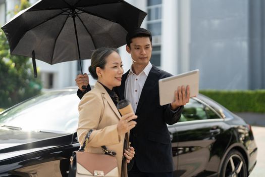 Portrait of young and senior business people working together with digital tablet at outdoor car park