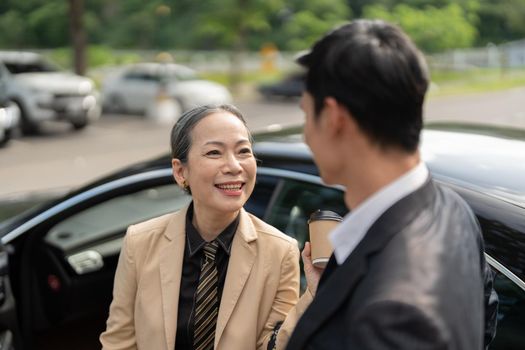 Happy senior old asian businesswoman discussion talking about new project with young asian male colleague at car park