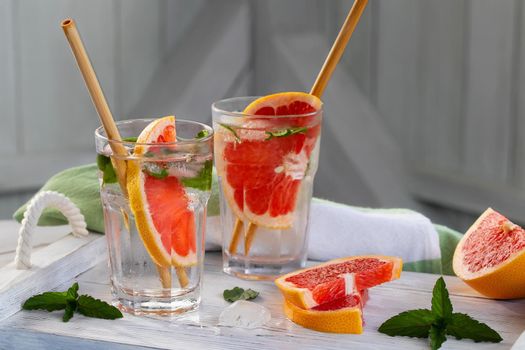 Summer refreshing cocktails with grapefruit slices and mint on a white wooden tray.
