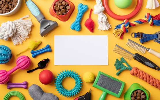 Pet care concept, various pet accessories and tools, toys, balls, brushes on yellow background with blank paper for mockup design, flat lay pattern